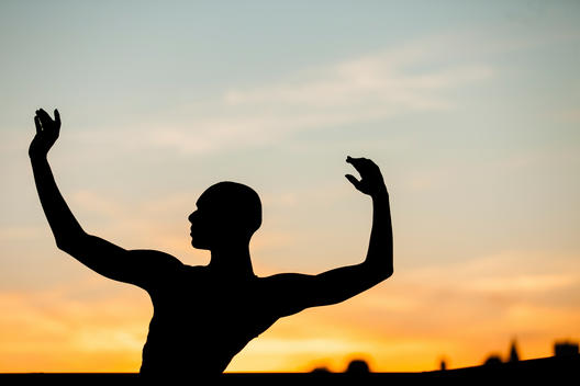 A dancer silhouetted against a sunset with his arms raised.