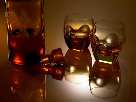 Still life of two glasses and bottle, all cognac colored on mirroring surface.