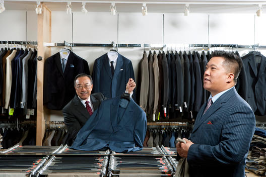 Jimmy Au holds up a jacket in his store while his son Allan holds a pair of pants