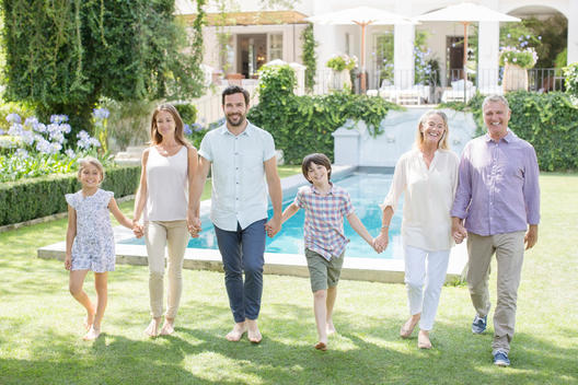 Multi-generation family holding hands and walking in backyard