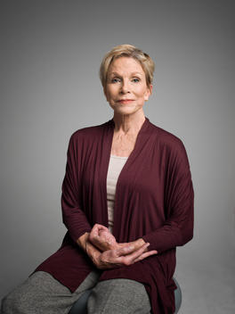 Woman in her 60\'s poses for a portrait siting on a stool