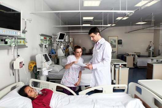 Doctor and Nurse are checking the medical reports of a sleeping patient in an emergency room.