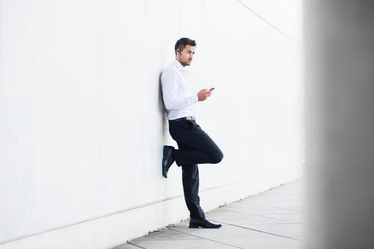 Young businessman leaning against wall texting on smartphone