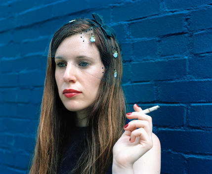 close-up of woman smoking, vintage hair net, in front of saturated blue wall