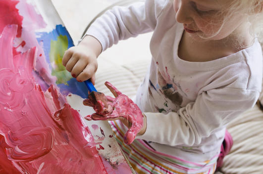 Young white blonde girl playing and finger painting with colorful paints