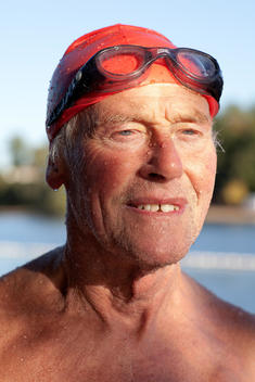A portrait of a mature male who is wet and has been swimming in a river, wearing a swimming cap.