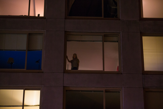 Outline of woman looking out window of apartment.