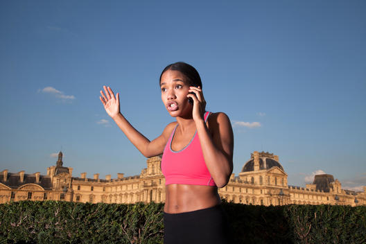 Athletic African woman using mobile phone, The Louvre in background