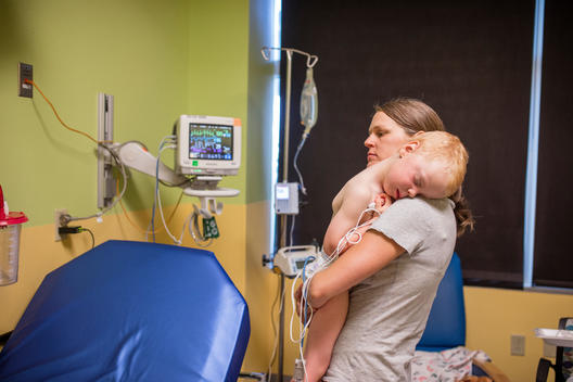 Grant, a young red-head boy, is hugged by his mother in the hospital, with tubes connected to his body, after nearly drowning in the pool before his mother pulled him out of the water. Heritage Hills, Colorado