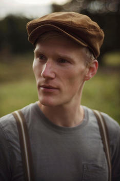 Close portrait of young man wearing a flat cap outdoors looking to the side