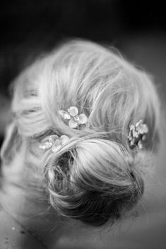 The back of a woman's head, her blonde hair pulled into a bun, with floral and diamond pins