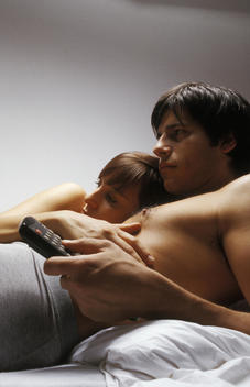 Young couple lying together in bed watching television