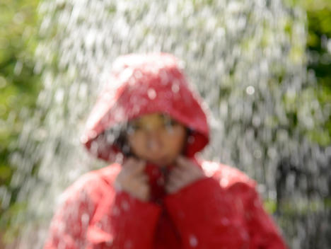 Blurred portrait of young woman wearing red hooded jacket standing in the rain