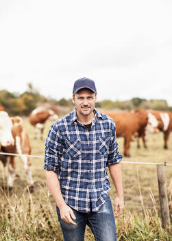 Portrait of confident farmer standing on field while animals grazing in background