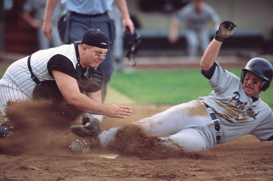 Baseball player sliding headfirst into catcher at home base