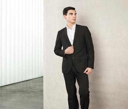 Fashion Portrait Of A Young European Male Model Wearing A Black Suit And A White Shirt, Standing Infront Of A Concrete Wall, Modern Architecture, He Has Brown Eyes And Dark Brown Short Hair