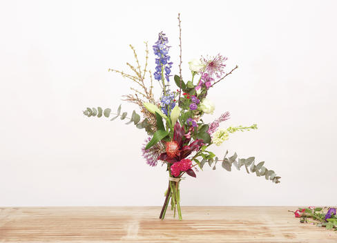 A bouquet of freshly flowers on a wooden table against a white background, cutting tools nearby.