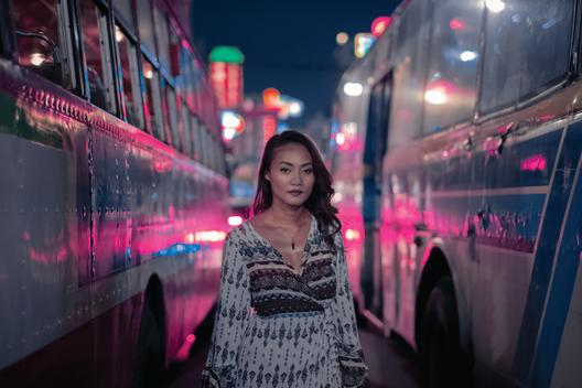 Portrait of a girl in between two bus at night in the streets of Bangkok, Thailand.