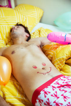Man with smiley face drawing on belly sleeping after party