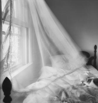 Curtain Blowing With The Wind Over An Unmade Bed.
