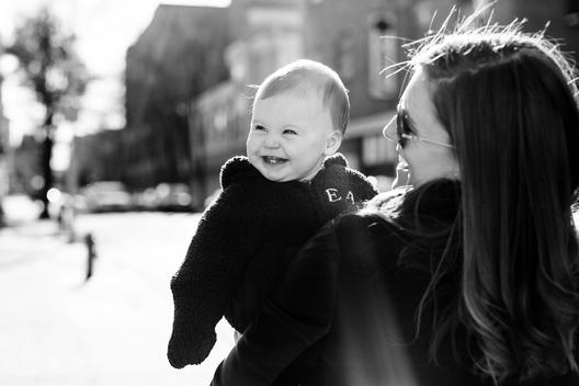 Black and white image of mom holding baby girl smiling in winter jacket