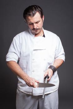 Studio portrait of mid adult male chef sharpening knife
