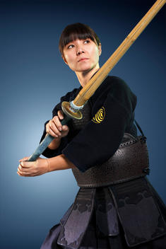 A female Asian Kendo fighter in her black Kendo uniform and armour holdng her Shinai weapon.