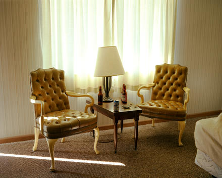 Two Brown Leather Chairs In Yellow Motel Room With Window And Strip Of Light