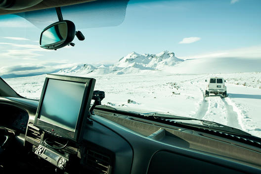 SUV interior with a GPS screen and a view through the windsheild of a truck, driving on a snowy glacier landscape in Iceland