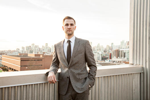 Portrait of man in suit outside with city skyline in background.