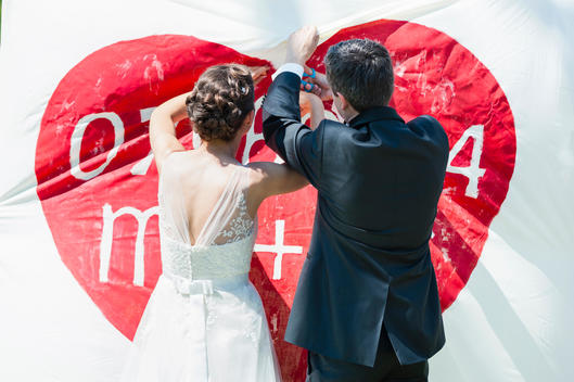 Rear view of bride and bridegroom hanging bespoke banner with red heart