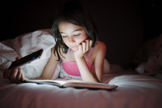 Mixed race girl reading by cell phone light in bed
