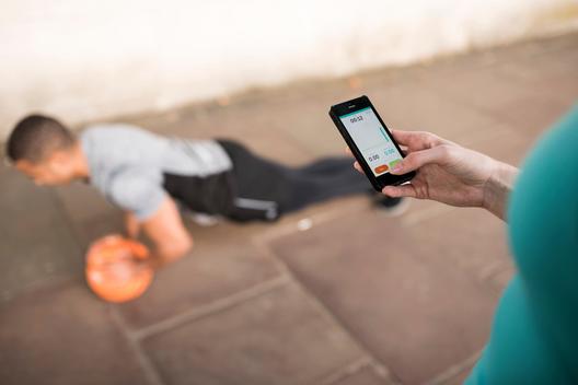 Over shoulder view of female trainer timing male runners push ups on smartphone