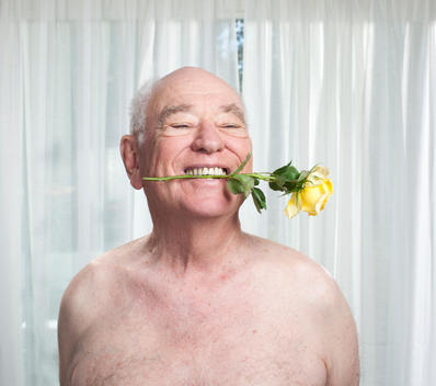 Close up of shirtless old man with rose in his mouth