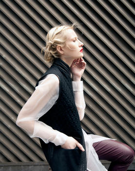 Profile of a woman wearing a black vest and maroon leather pants against a striped wall.