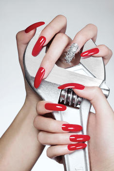hand with long red nails and one nail, ring finger, carrying special silver decorations. The hand grabs around a large metal rig, published in nail it magazine