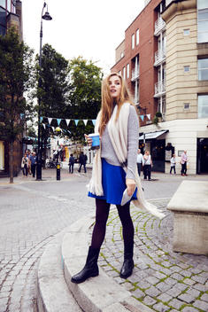 editorial street style shoot with model wearing a blue skirt and grey sweaterh holding a coffee cup