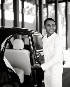 A Smiling Doorman Warmly Opens A Car Door For A Guest.