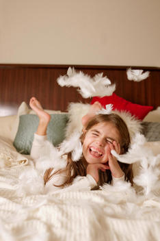 laughing girl on bed surrounded by flying feathers