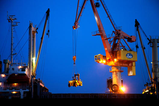 A crane on a cargo ship lifts a new forklift for delivery.