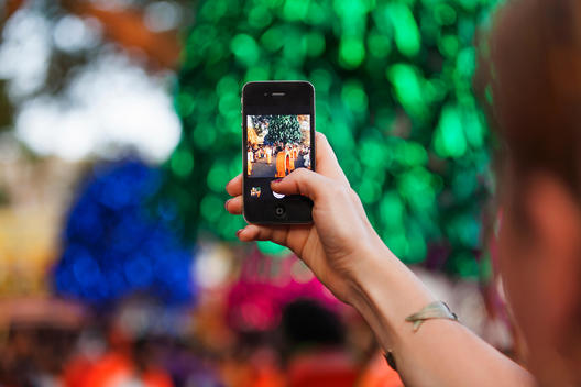 Woman holding up smart phone to take a picture of carnival in Kochi, Kerala, India