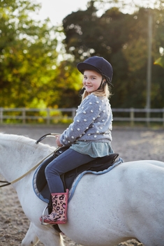 Portrait of happy girl riding white pony in equestrian arena