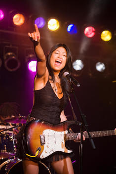 Asian woman singing and playing electric guitar onstage