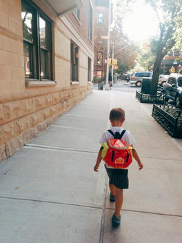 A boy with a backpack walking down the street on his first day of school.