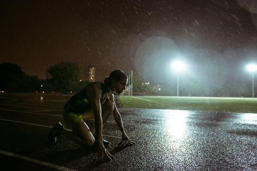 A female athlete prepping to run in the rain at night on a football field.