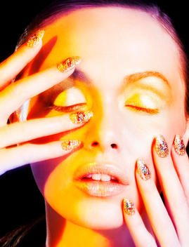hands with elaborate nails with crystals photographed with Long time exposure and yellow lighting of a close up of a face, shot for Nail it published in Zink Magazine