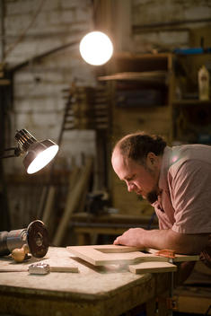 An Amish Man Works In The Woodshop With A Work Lamp.