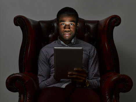 Portrait of sinister young man in armchair with digital tablet