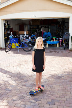girl standing on a skateboard in the driveway of her home