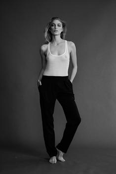 Fashion model with tank top tucked into black pants lightly seeing chest underneath shot in studio on grey.